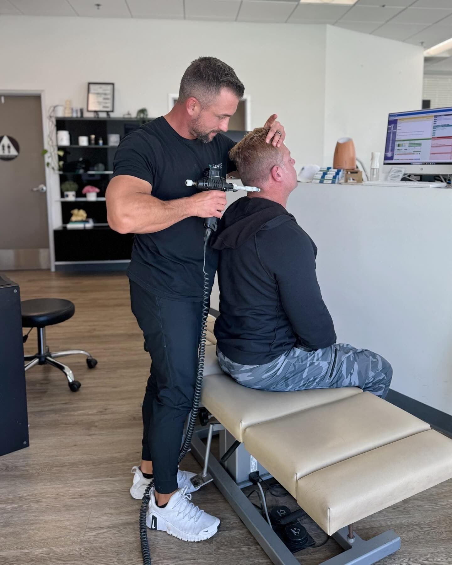An Element Wellness Center chiropractor performing an instrument-assisted adjustment at the base of a patient’s neck